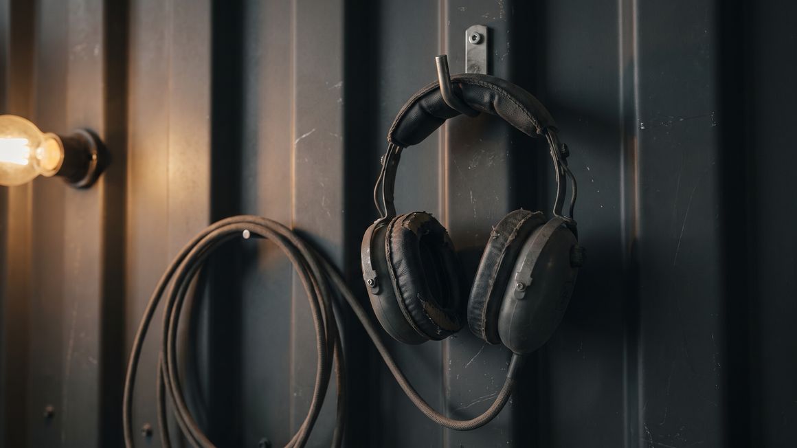 A worn aviation headset hanging on a hook against a dark hangar wall